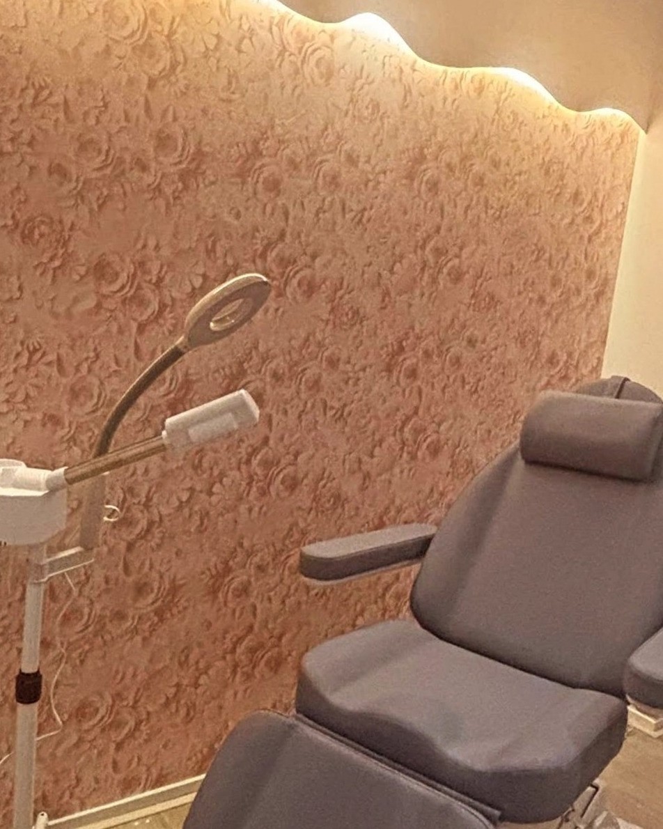 De behandelkamer van Éclat by Sali: behandelstoel, loeplamp en stomer voor een rozenwand met warm licht