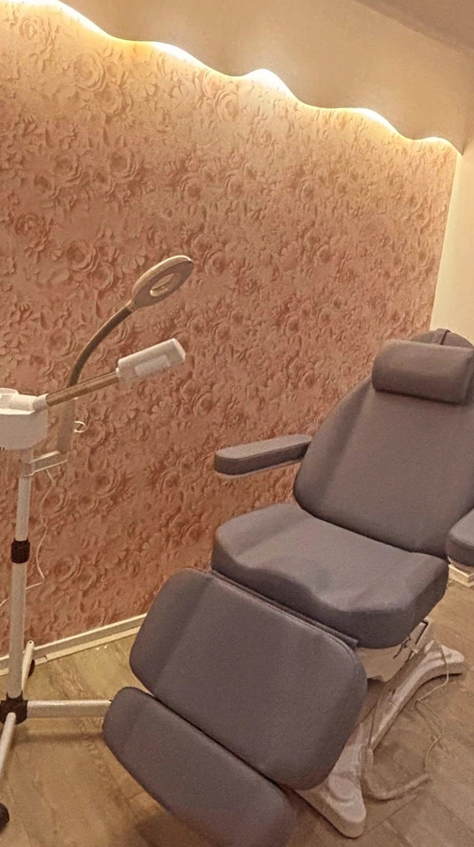 De behandelkamer: grijze behandelstoel, loeplamp en stomer, een wand met reliëfrozen en een golvende lichtlijn erboven